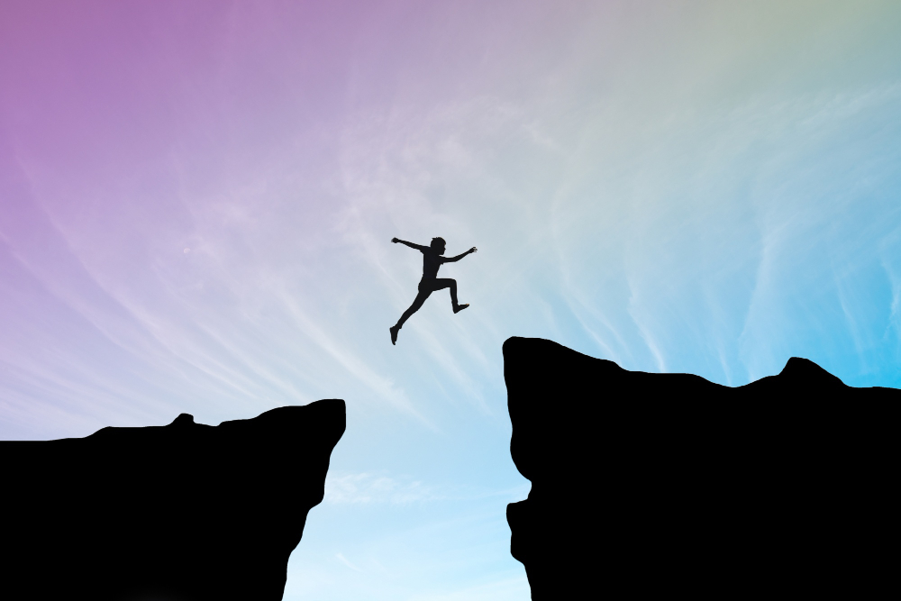 A person taking a risk by jumping from one cliff to another.